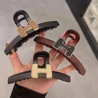 a person holding three hair clips with the letter h on them